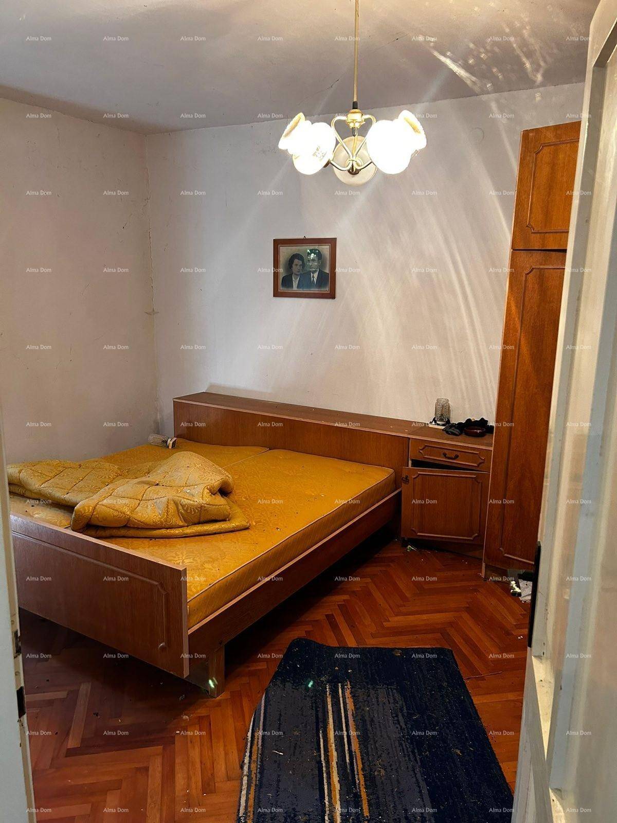 Schlafzimmer mit Holzbett, Kleiderschrank und Fischgrätparkettboden unter einer Deckenleuchte.