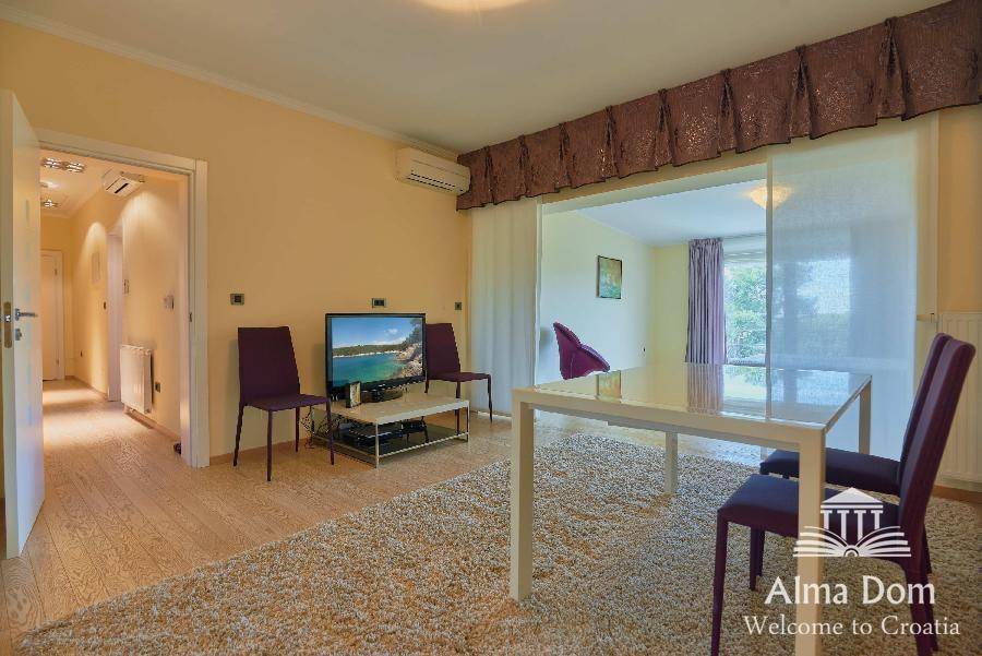 Offener Wohn- und Essbereich mit Teppichboden, Fernseher und Zugang zu einem weiteren Zimmer.