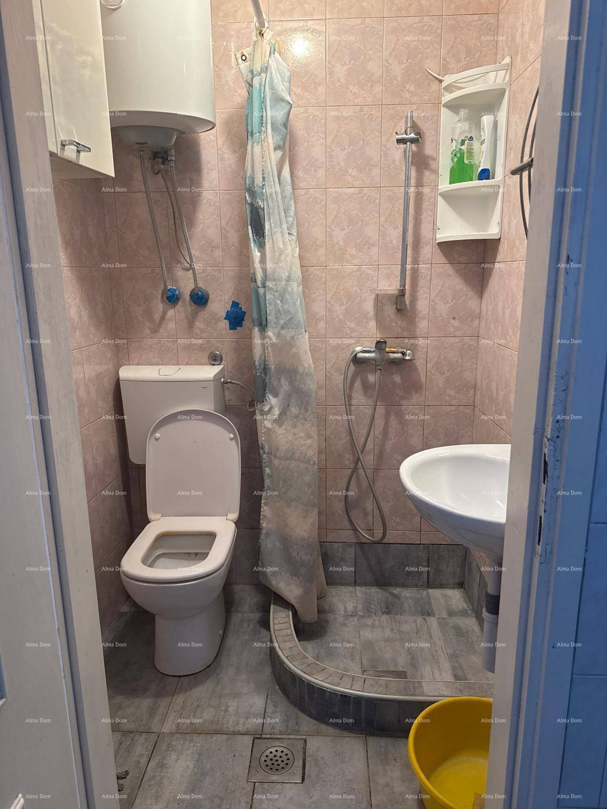 Kleines Badezimmer mit rosa Fliesen, Toilette, Waschbecken und Duschbereich mit Vorhang.