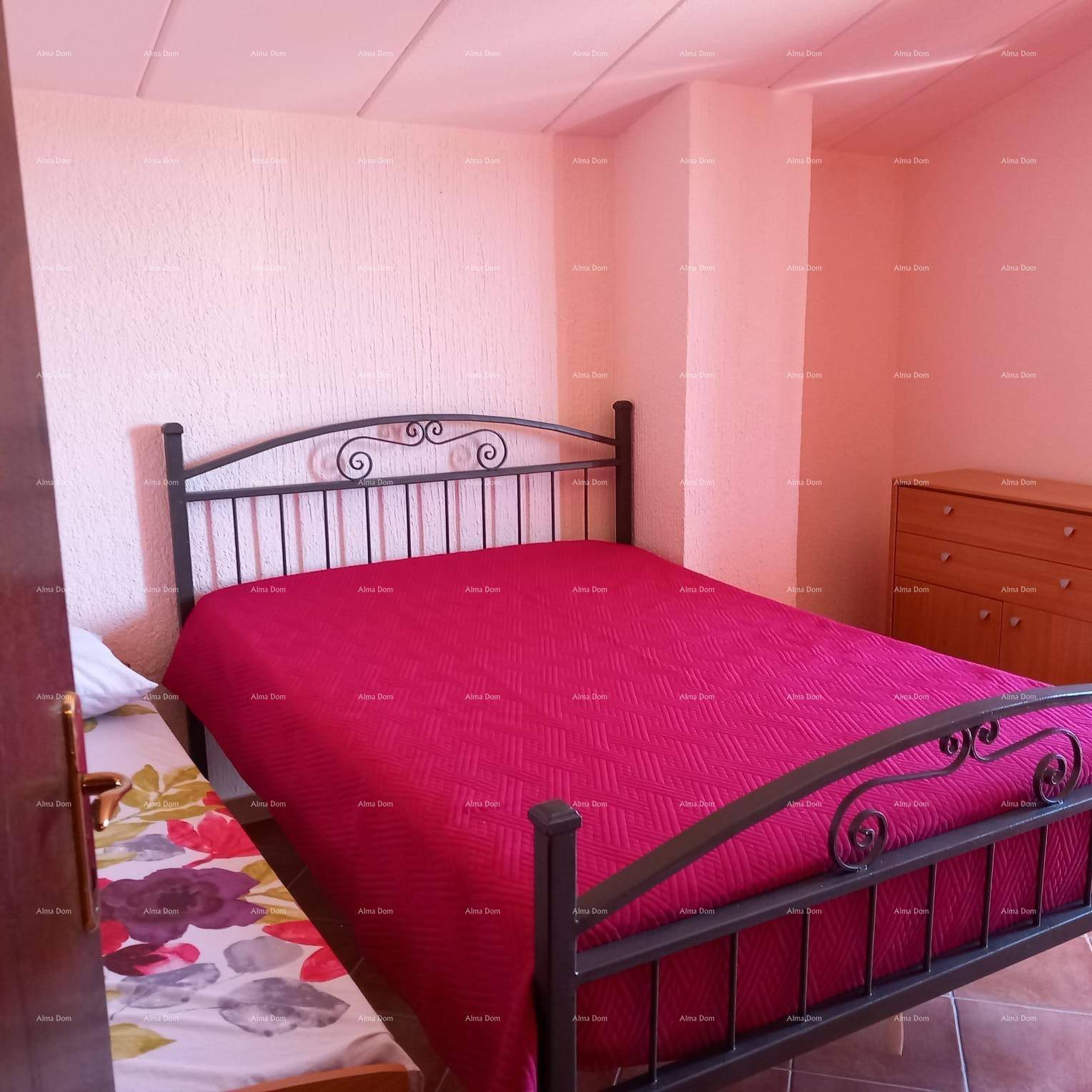 Schlafzimmer mit Metallbett, roter Bettdecke und Fliesenboden.