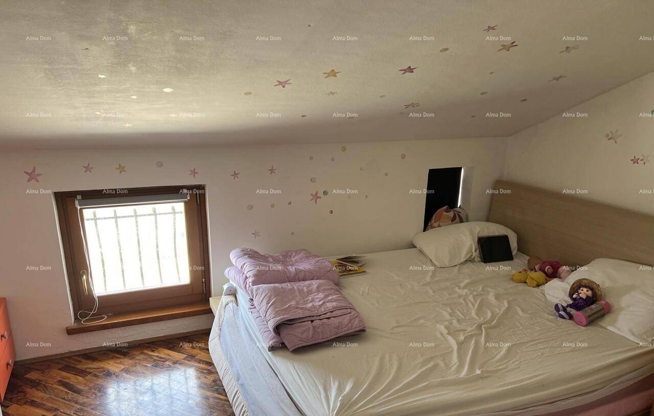 Gemütliches Schlafzimmer im Dachgeschoss mit schrägen Wänden, Holzboden und einem Fenster mit Gitter.