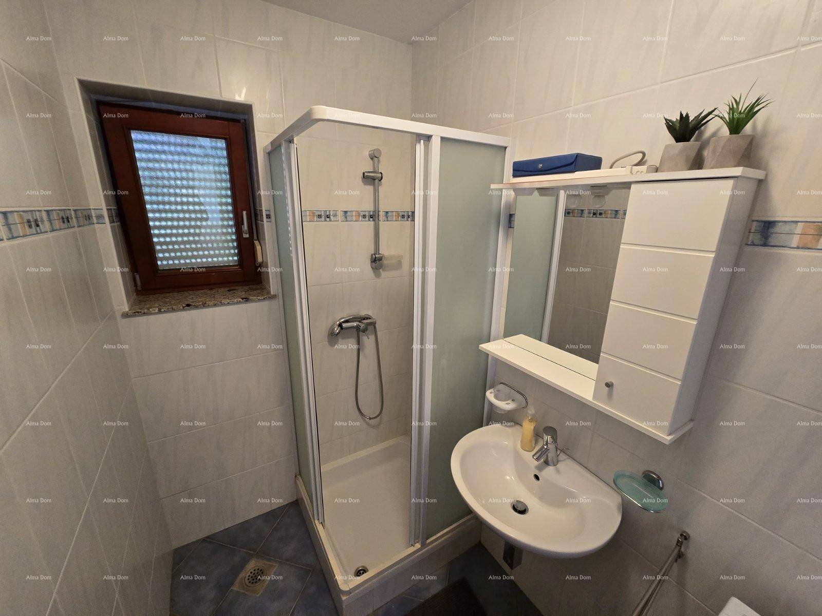 Badezimmer mit Duschkabine, Waschbecken, Spiegelschrank und einem Fenster mit Jalousien.