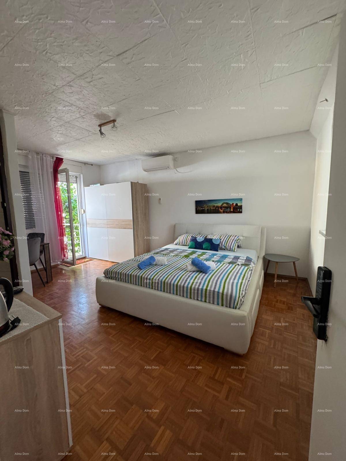 Schlafzimmer mit Doppelbett, Parkettboden und Zugang zu einem Balkon mit roten Vorhängen.