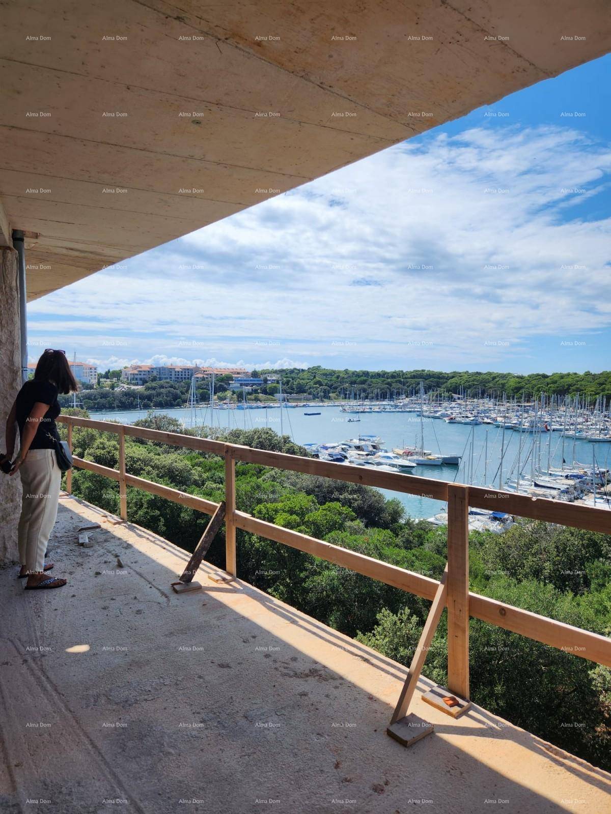 Person auf einem unfertigen Balkon genießt den weiten Blick auf den Yachthafen und die grüne Küste.