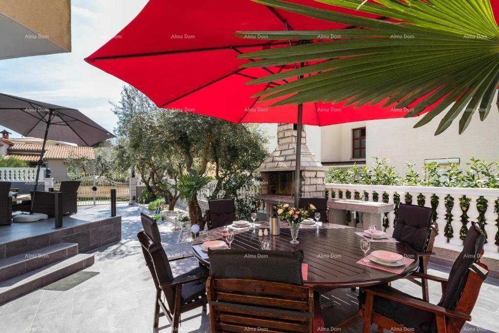 Sonniger Terrassenbereich mit großem Esstisch, rotem Sonnenschirm und gemauertem Grill für gesellige Abende.