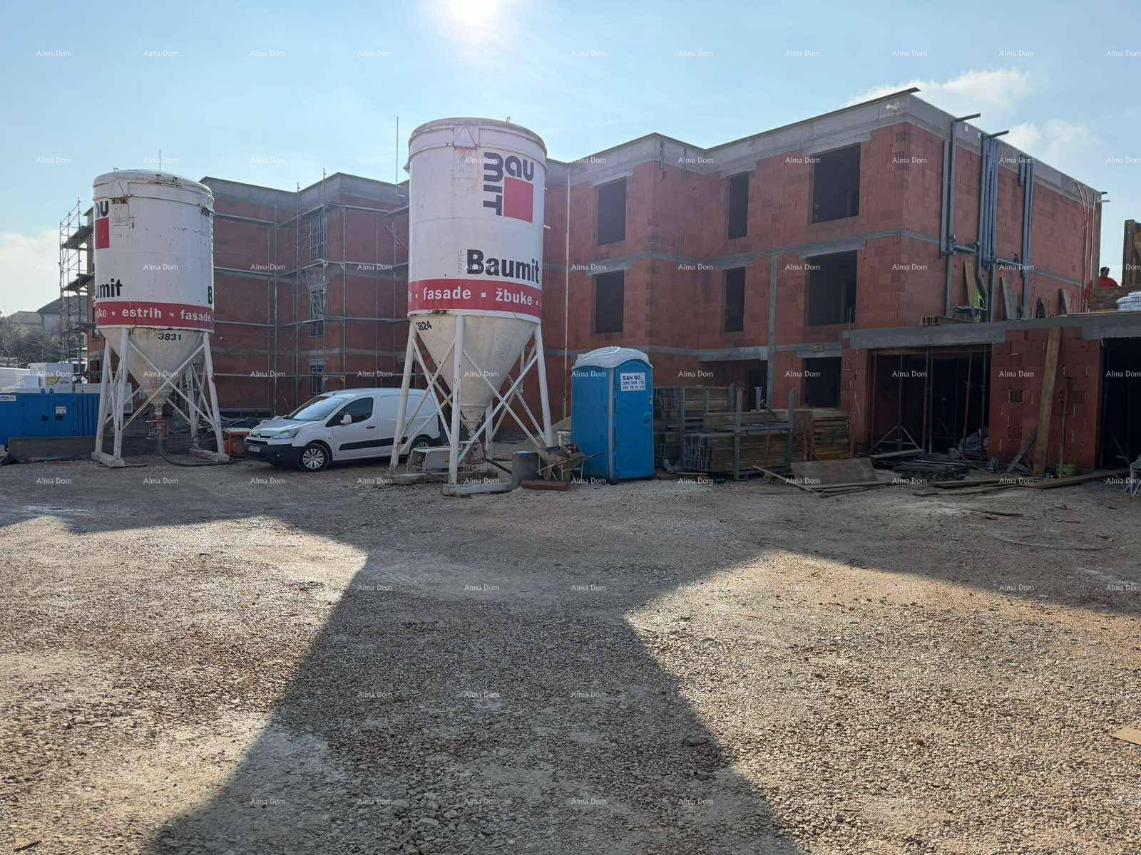 Baustelle eines Mehrfamilienhauses mit großen Silos und unfertigen Gebäudestrukturen unter blauem Himmel.