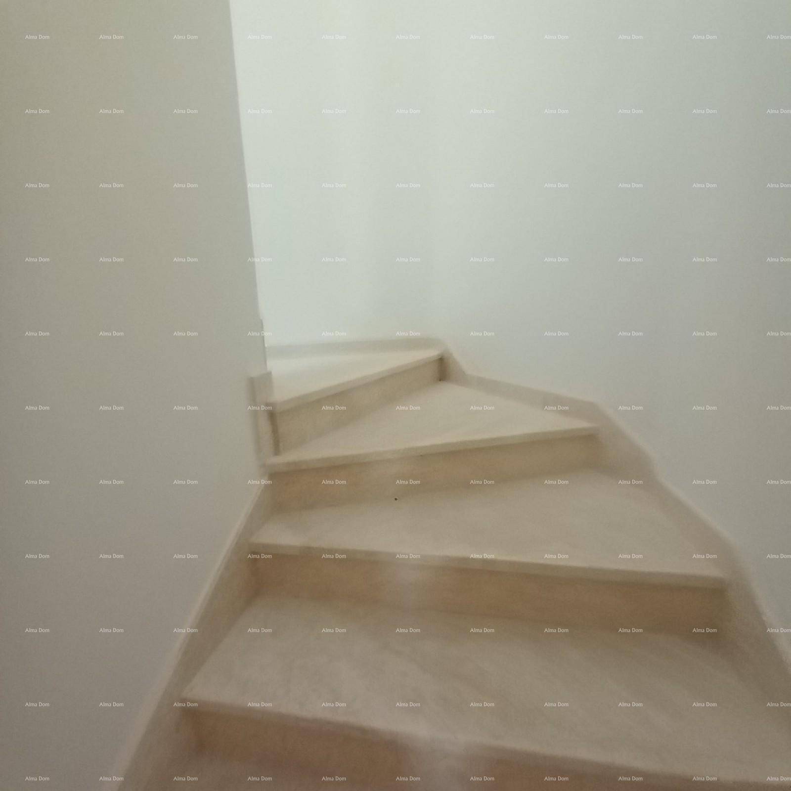 Treppenhaus mit hellen Stufen und weiß gestrichenen Wänden, die zu einem oberen Stockwerk führen.