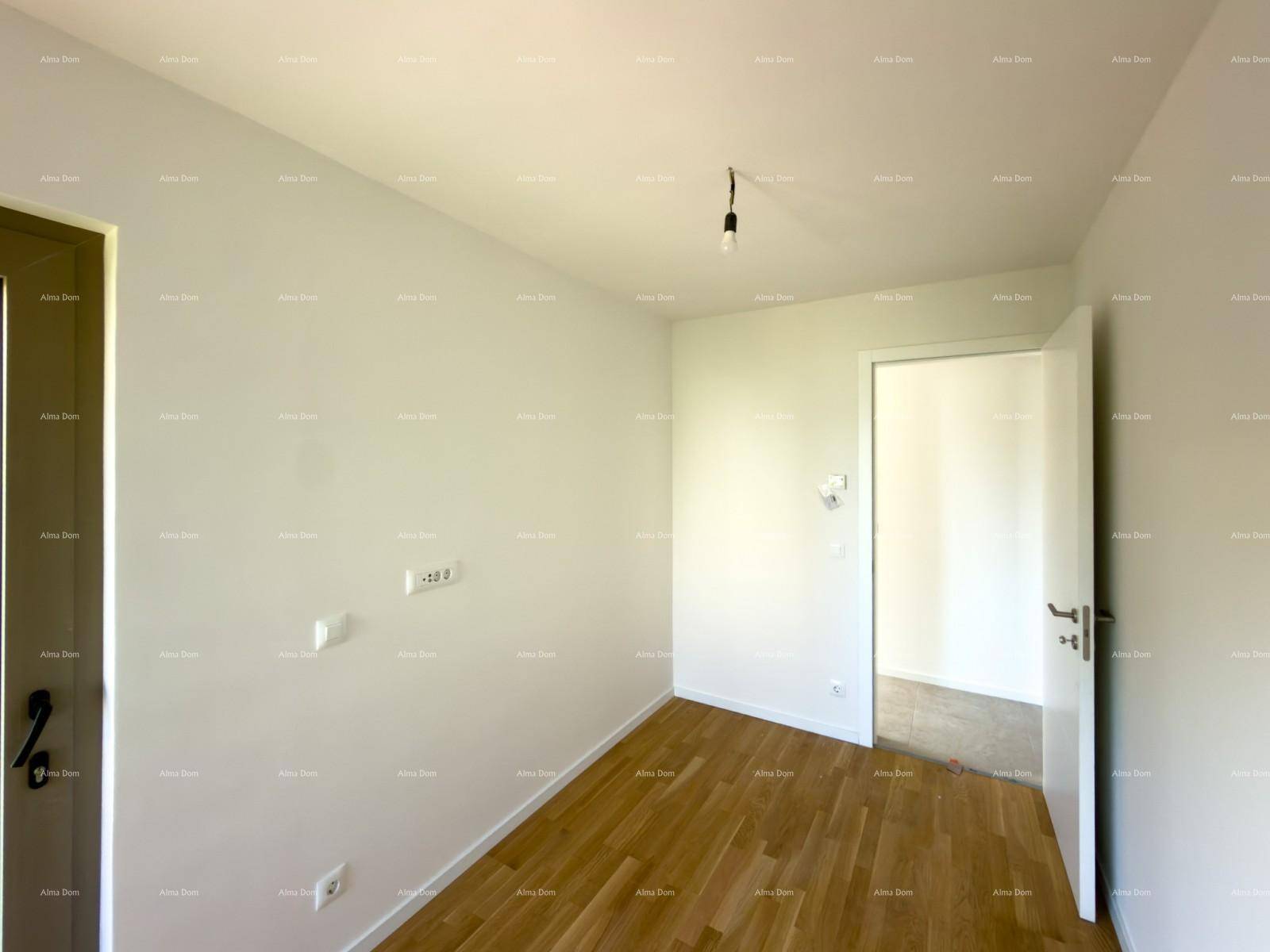 Helles Zimmer mit Holzboden und weiß gestrichenen Wänden, eine offene Tür führt in einen weiteren Bereich.