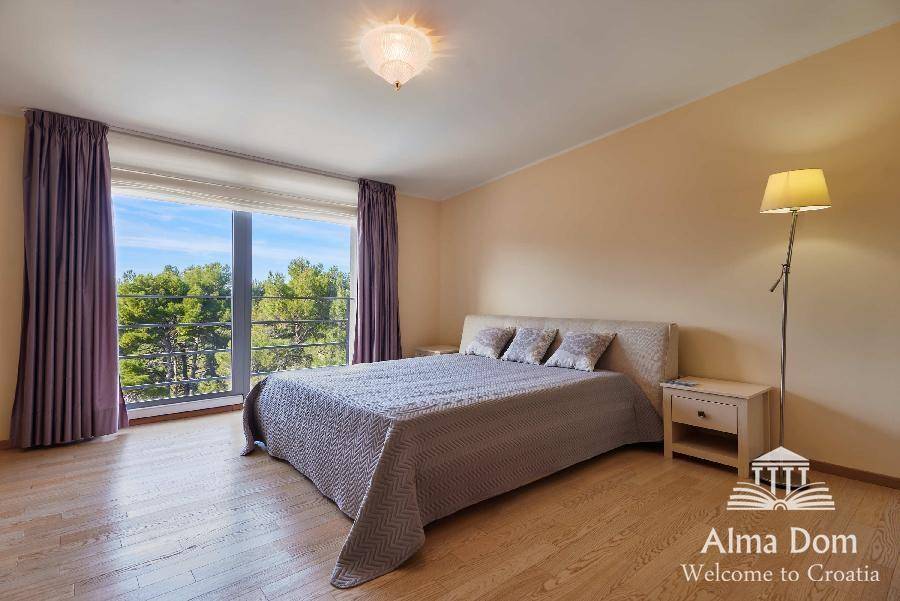 Helles Schlafzimmer mit Holzboden, großem Fenster und weitem Blick auf die grüne Umgebung.