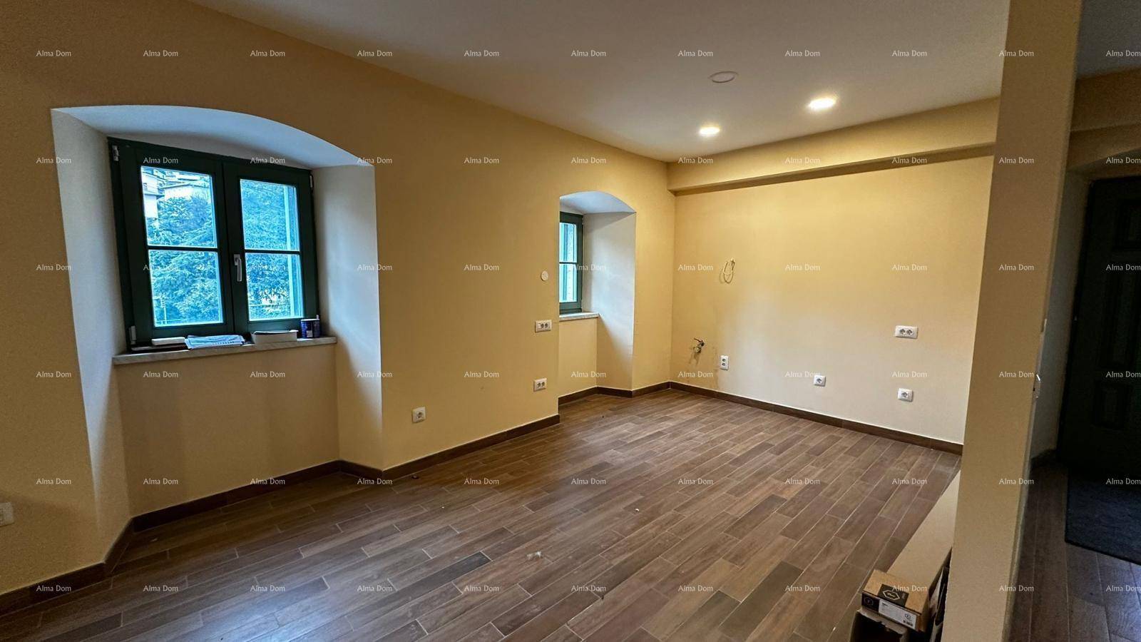 Großer Wohnraum mit Holzfliesenboden, zwei Fenstern und heller Wandfarbe.