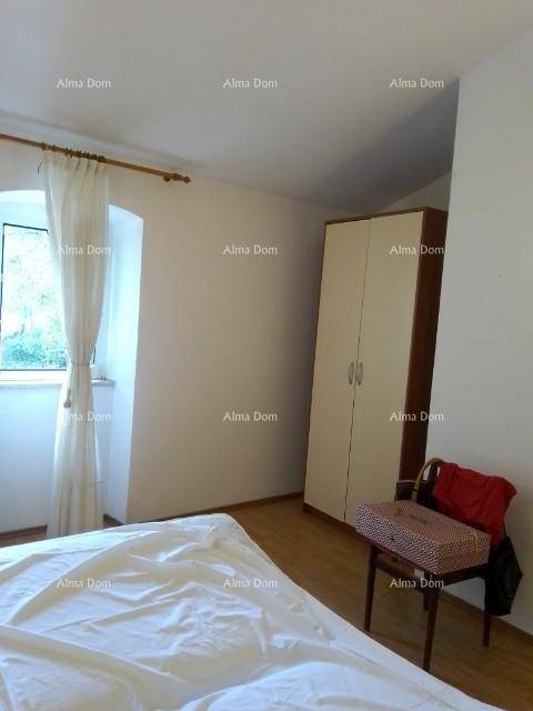 Schlafzimmer mit Bett, Kleiderschrank und einem Fenster mit Vorhängen, auf Holzboden.