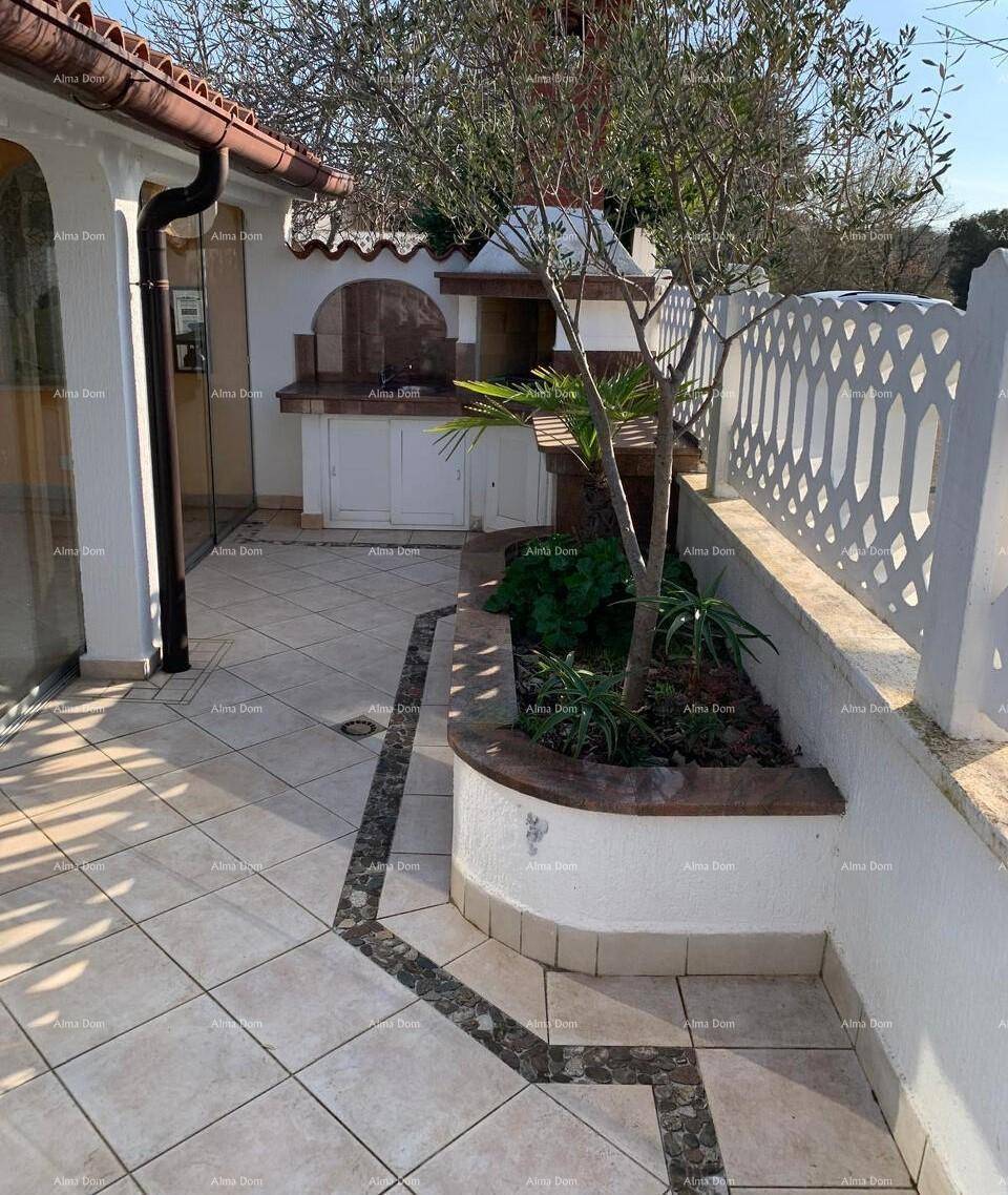 Sonniger Terrassenbereich mit Außenküche und Grill, umgeben von mediterranen Pflanzen und einer dekorativen Mauer.