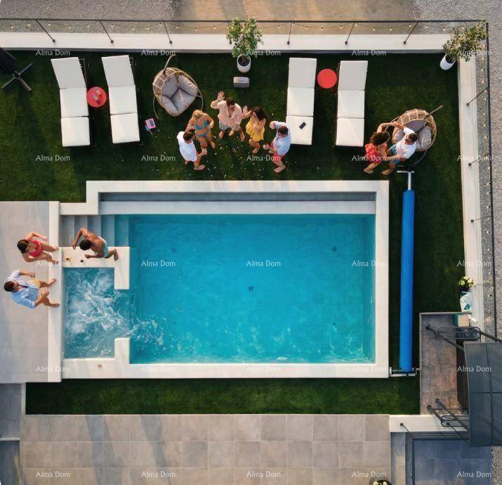 Luftaufnahme des Pools mit integriertem Whirlpool, umgeben von Sonnenliegen und Kunstrasen.