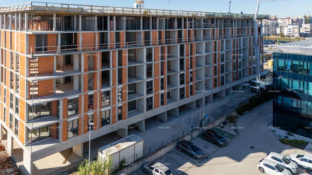 Ansicht eines im Bau befindlichen Gebäudes mit Parkplätzen und angrenzenden modernen Bürogebäuden.