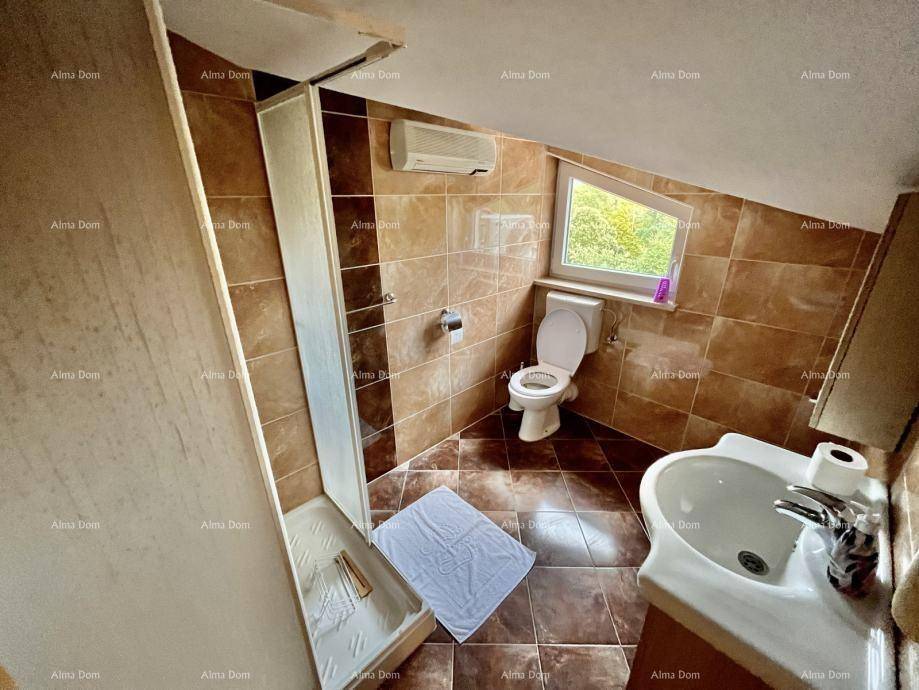 Badezimmer im Dachgeschoss mit Dusche, WC, Waschbecken und Dachfenster, gefliest in Braun.