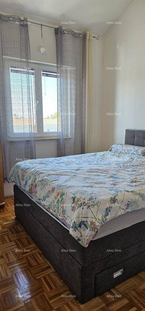 Schlafzimmer mit Doppelbett, Fenster und gemusterten Vorhängen sowie Parkettboden.