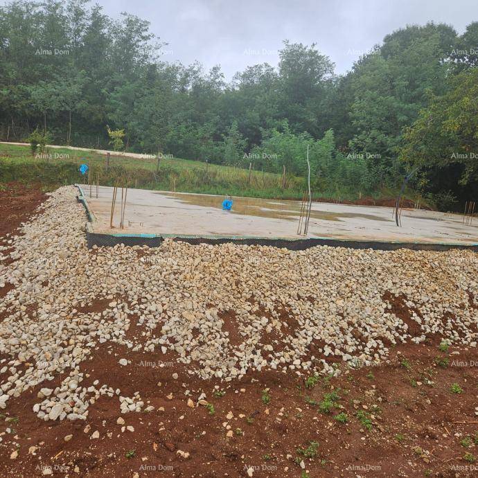 Fundamentplatte einer neuen Baustelle, umgeben von Schotter und Erde, mit Wald im Hintergrund.
