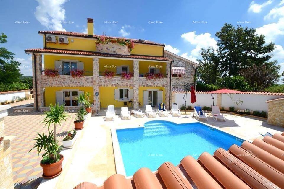 Gelbe Villa mit Poolbereich, Sonnenliegen und blühenden Pflanzen.