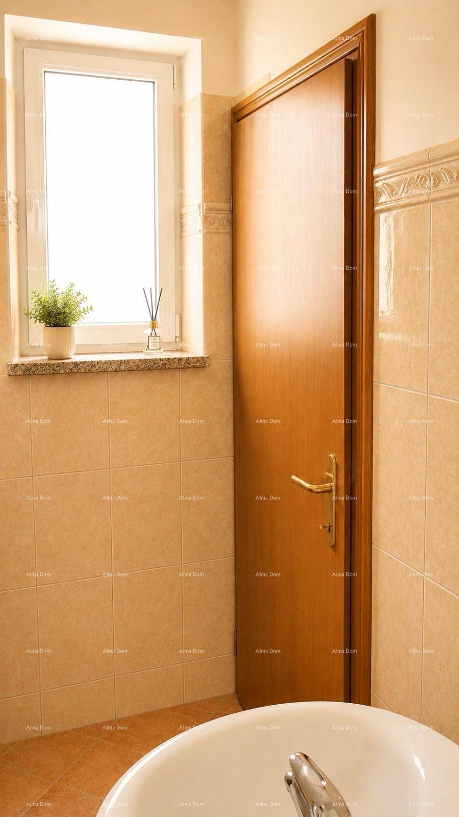 Helles Badezimmer mit beigen Fliesen, Fenster und einem Waschbecken.