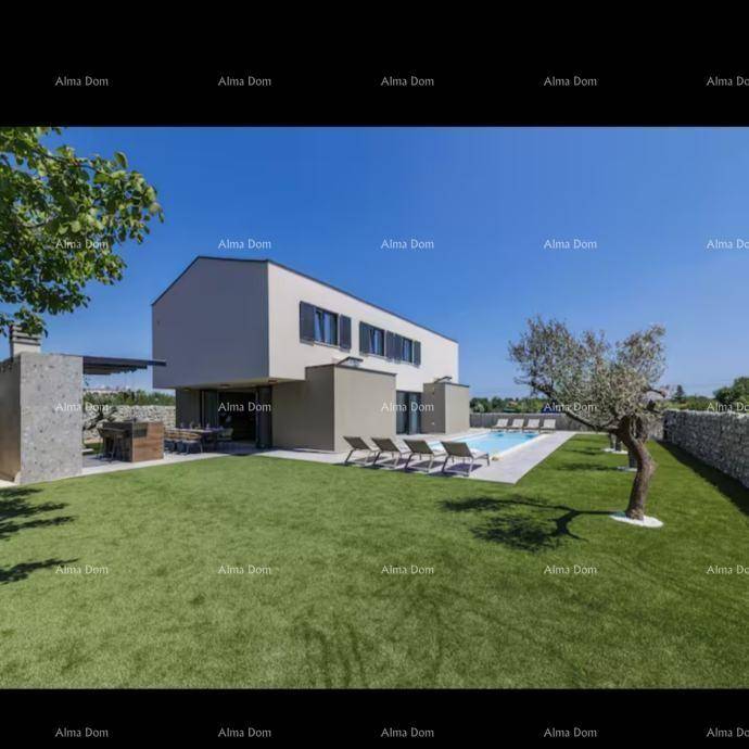 Seitliche Ansicht der modernen Villa mit großem Rasen, Pool und Steinmauer unter strahlend blauem Himmel.