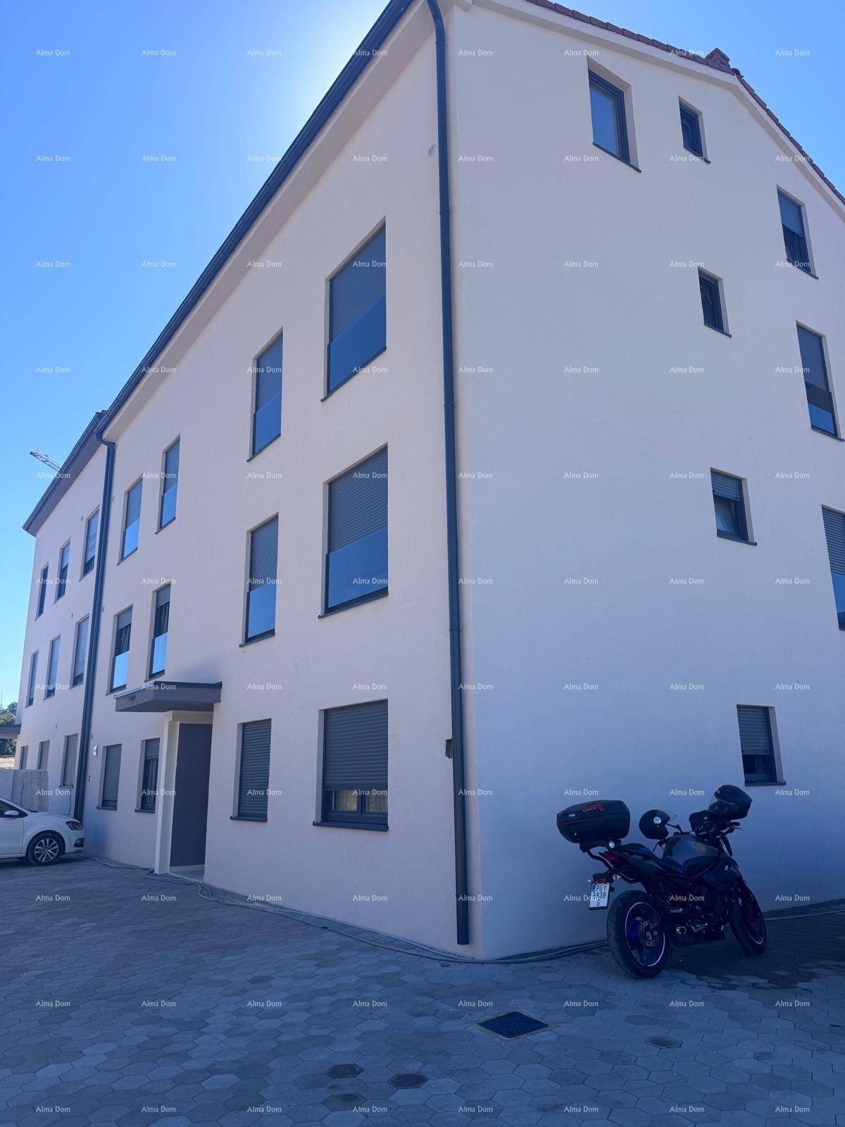 Moderne Gebäudefassade mit hellen Wänden, dunklen Fensterrahmen und gepflastertem Vorplatz.
