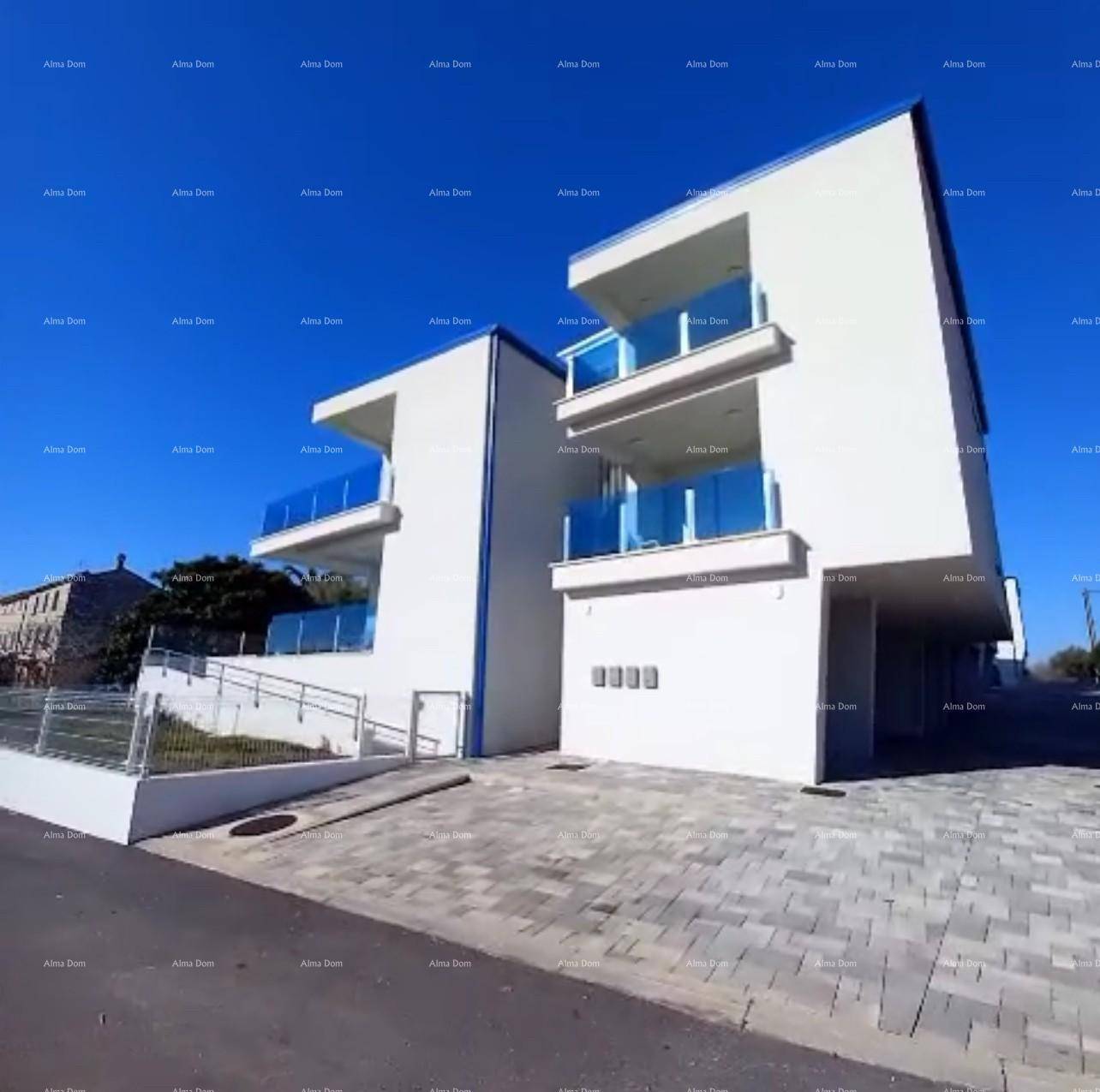 Modernes weißes Gebäude mit blauen Glasbalkonen, gepflastertem Vorplatz und Rampe.