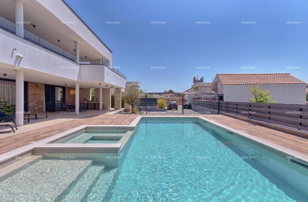 Weitläufiger Poolbereich mit Holzdeck und moderner Villa im Hintergrund unter blauem Himmel.