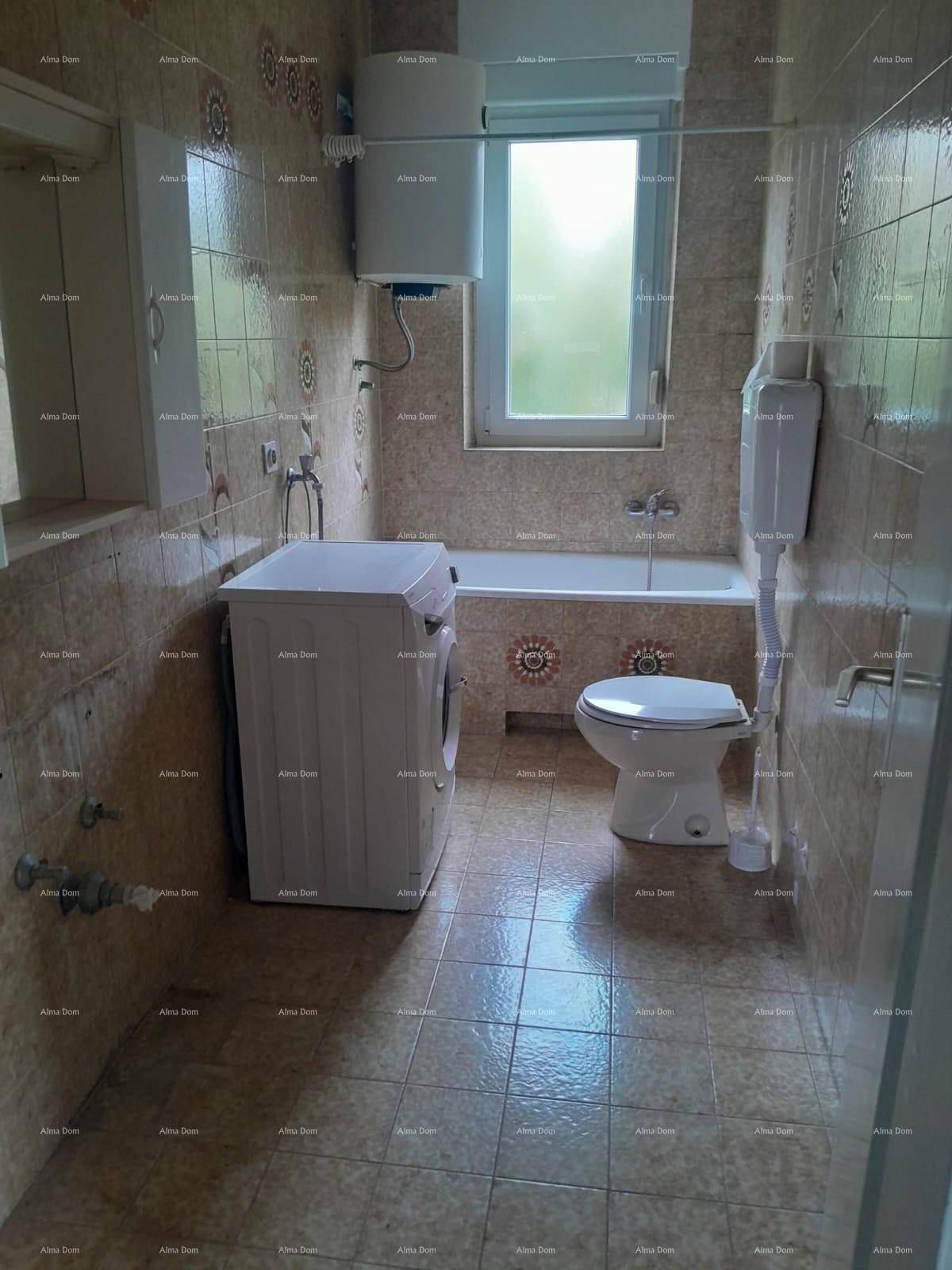 Badezimmer mit gemusterten Fliesen, Badewanne, Toilette, Waschmaschine und Fenster.