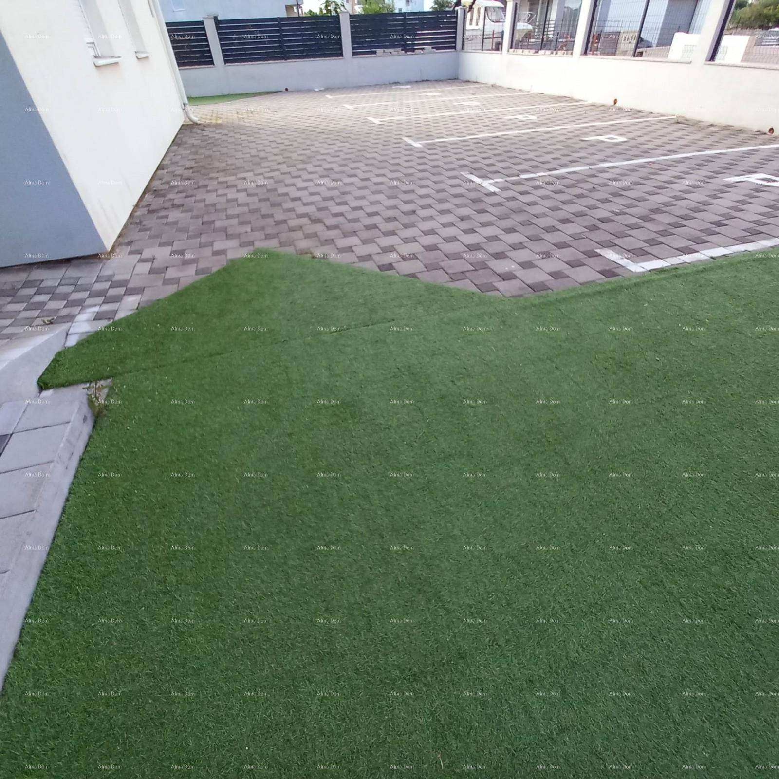 Außenbereich mit Kunstrasen und gepflasterten Parkplätzen neben dem Gebäude, ordentlich und funktional.