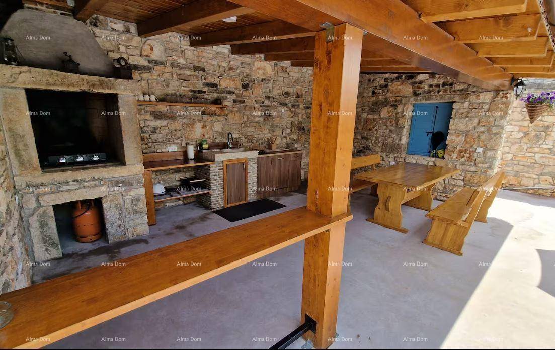 Rustikale Außenküche mit Grill, Holztisch und Bänken unter einer überdachten Holzkonstruktion.