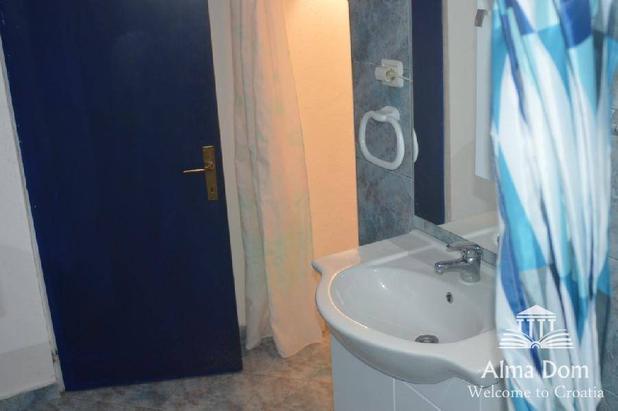 Einfaches Badezimmer mit Waschbecken, Spiegel und blau-weißem Duschvorhang.
