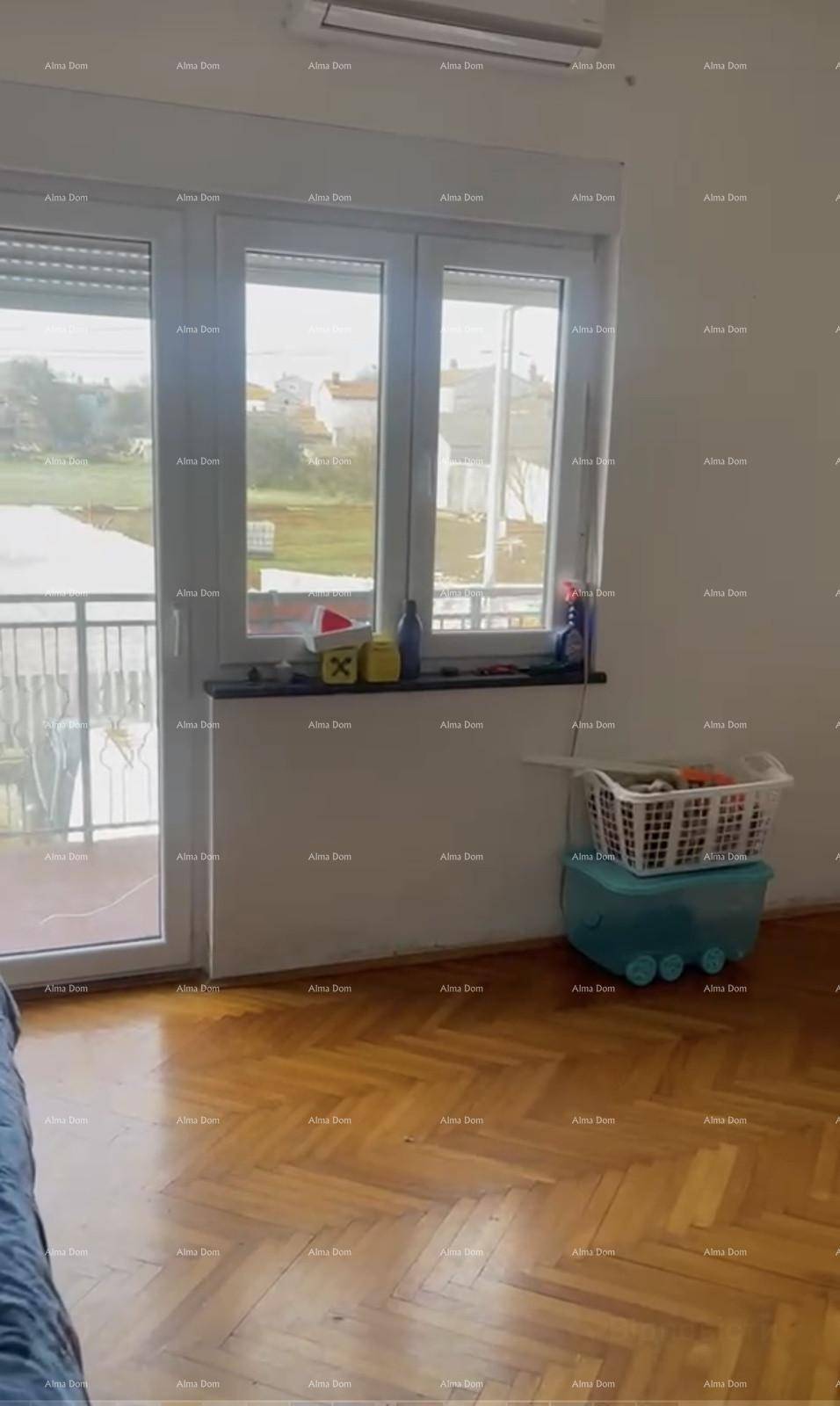 Blick aus dem Innenraum durch große Fenster auf einen Balkon mit grüner Aussicht.