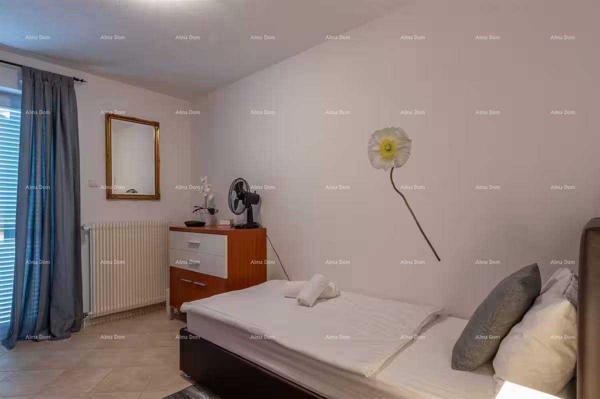 Schlafzimmer mit Einzelbett, Kommode, Ventilator und Fenster mit Jalousien.