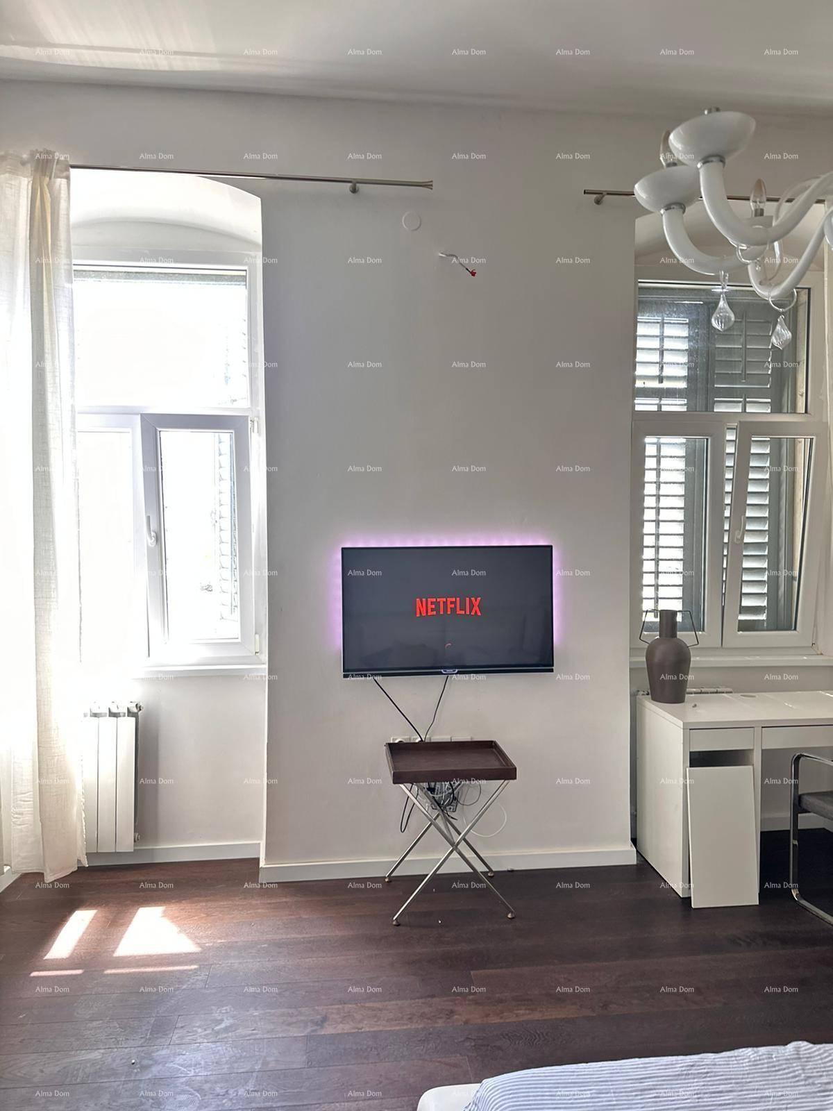 Schlafzimmer mit Wandfernseher, Schreibtisch und großen Fenstern für viel Tageslicht.