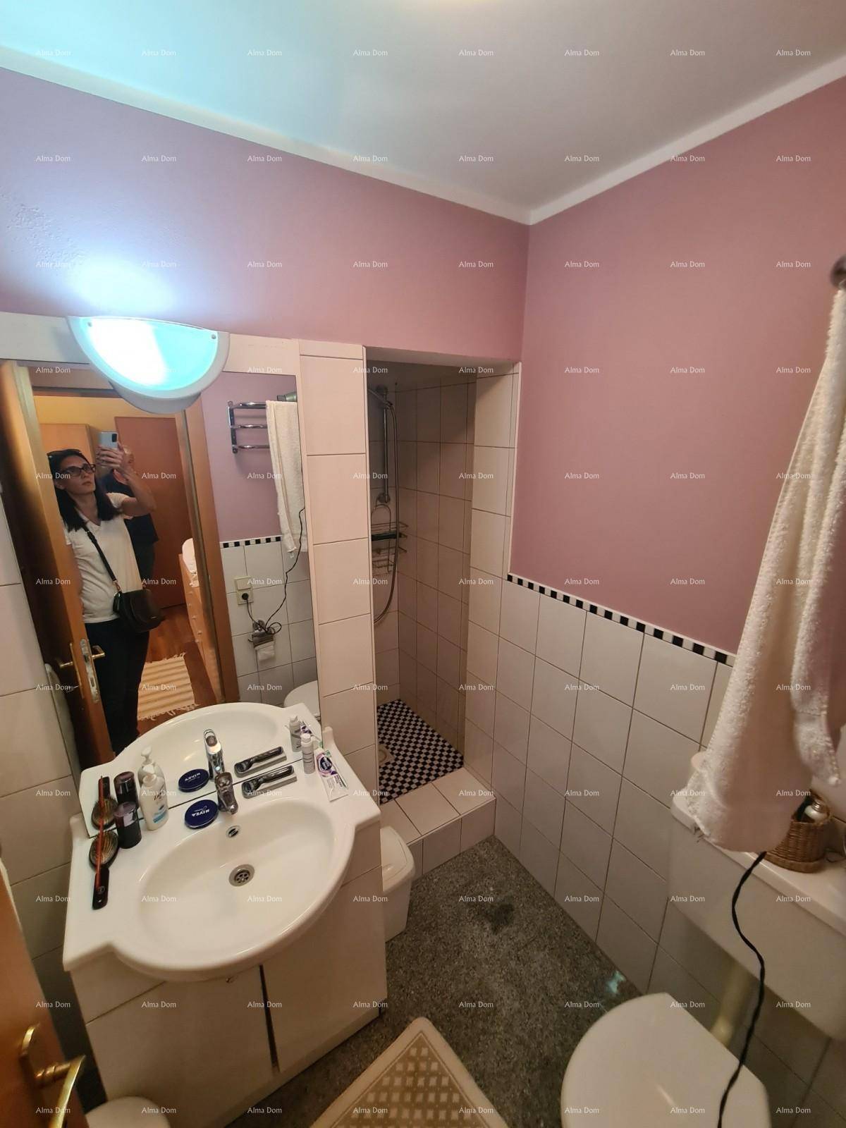 Badezimmer mit Waschbecken, Toilette und Duschbereich, ausgestattet mit rosa und weißen Fliesen.
