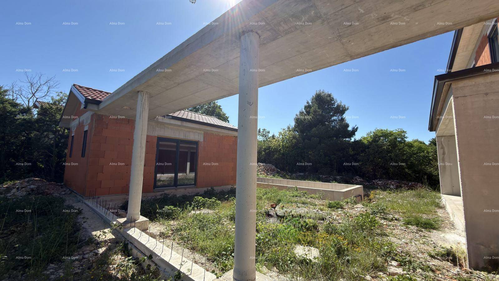 Baustelle eines Hauses mit freistehenden Betonsäulen und unberührter Natur im Hintergrund.