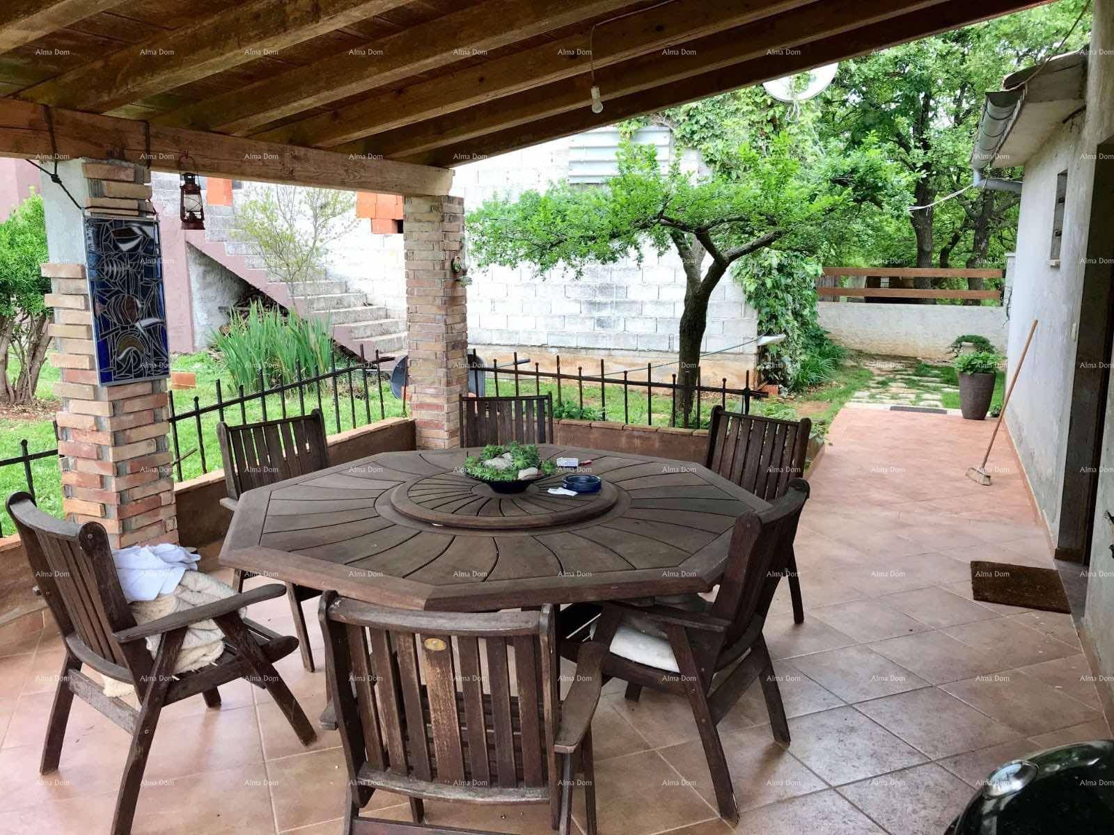 Gemütliche überdachte Terrasse mit großem Holztisch und Stühlen, umgeben von Grün.