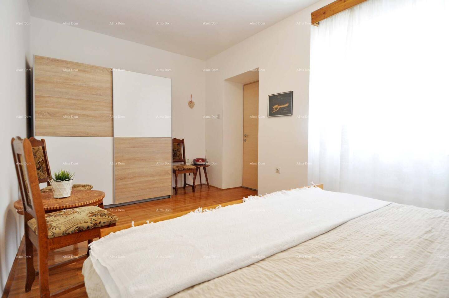 Schlafzimmer mit Doppelbett, Holzschrank und Fenster, das viel Licht hereinlässt.