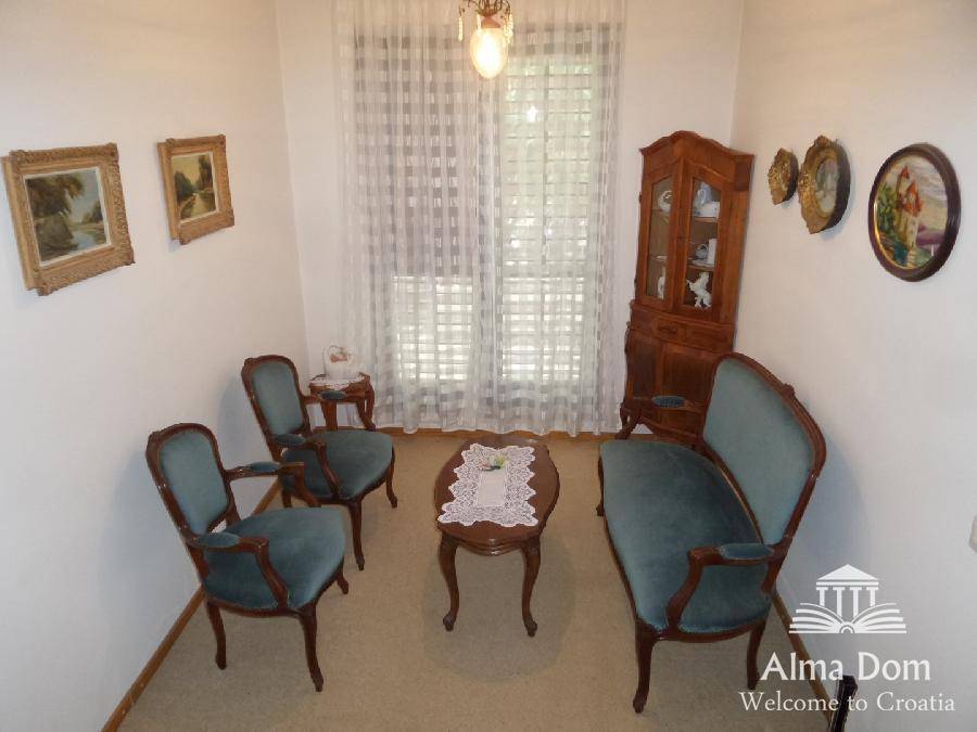Gemütliches Wohnzimmer mit antiken Möbeln, Teppichboden und großen Fenstern, hell und einladend.