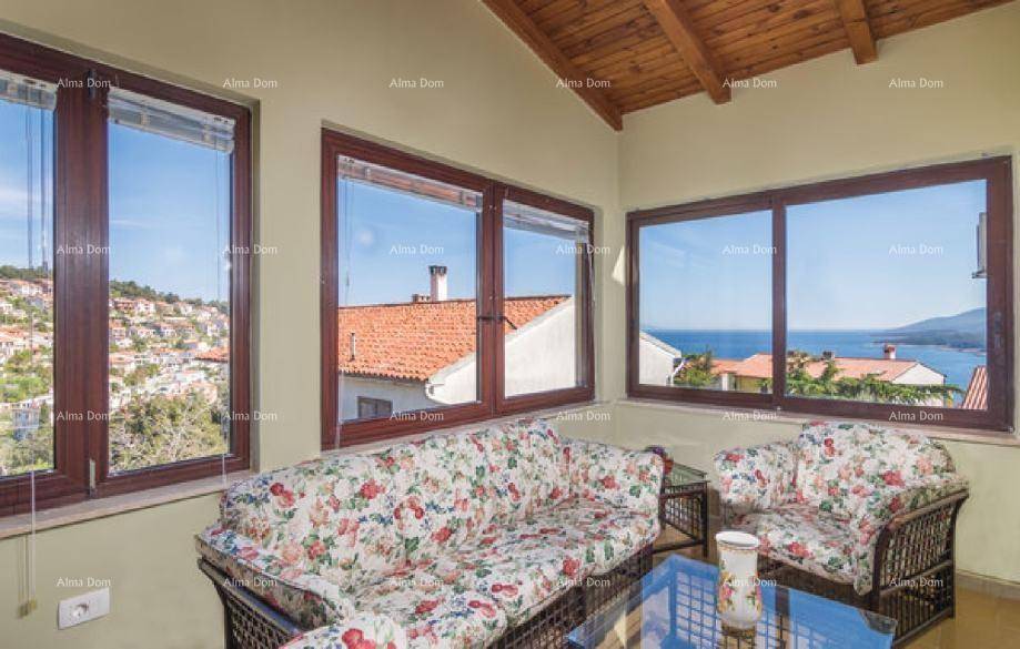 Gemütlicher Wohnbereich mit Korbmöbeln, Holzdach und großen Fenstern mit Blick auf die Umgebung und das Meer.