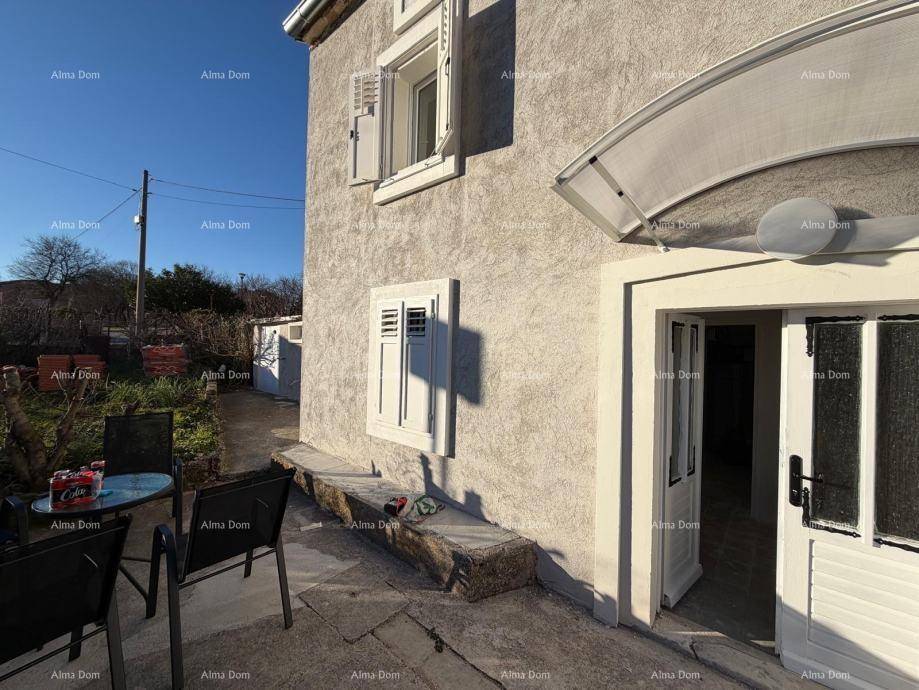 Kleine Terrasse am Hauseingang mit Sitzgelegenheiten und einer Steinbank unter blauem Himmel.