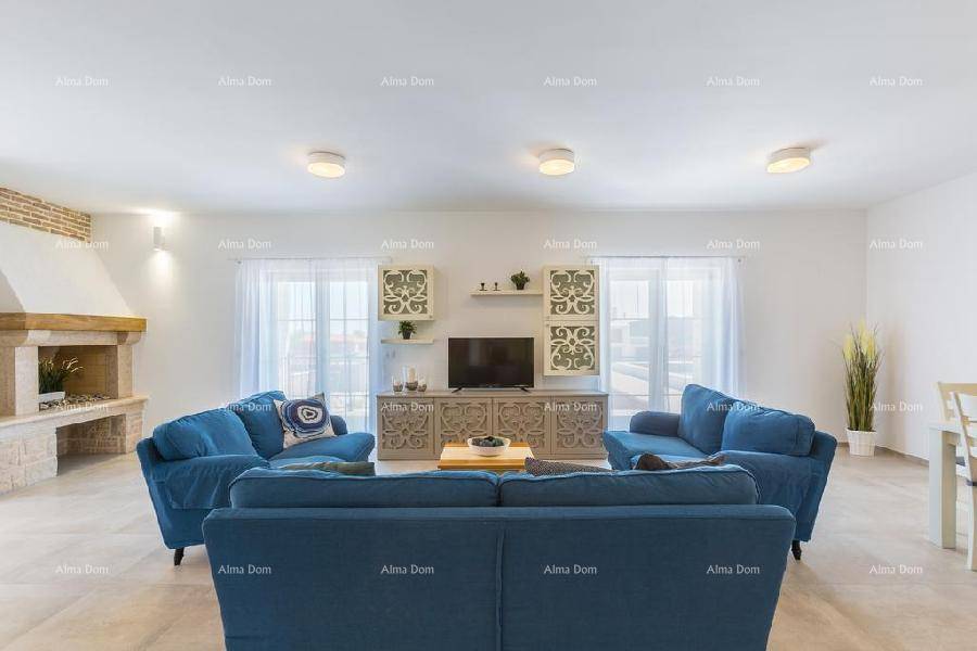 Gemütliches Wohnzimmer mit Kamin, blauen Sofas und Blick ins Grüne durch die großen Fenster.