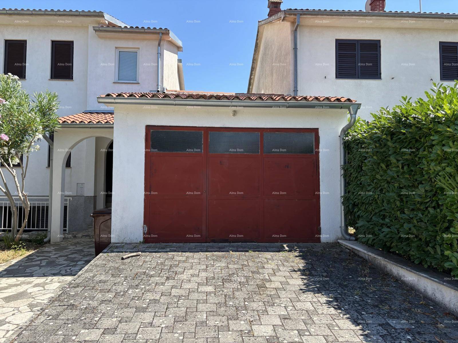 Garage mit rotem Tor und gepflasterter Einfahrt, umgeben von einer grünen Hecke.
