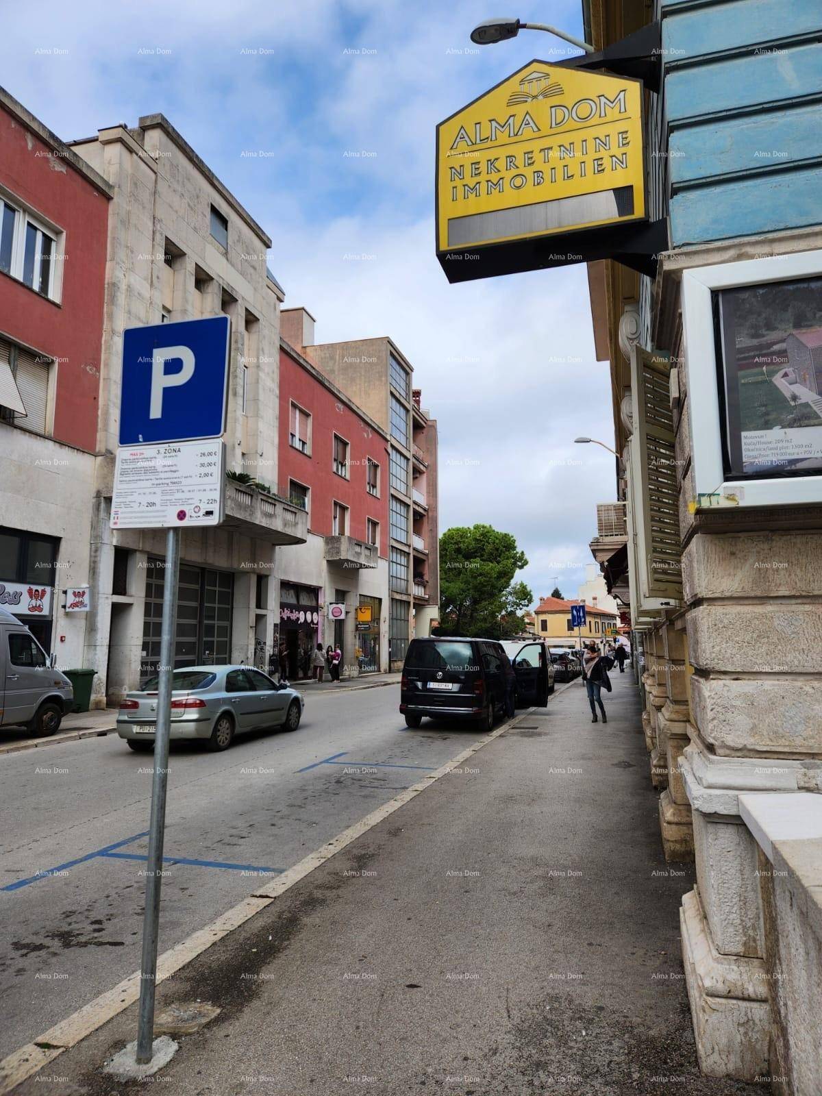 Belebtes Stadtbild mit Gebäuden, geparkten Autos und einem Immobilienmakler-Schild an der Straße.