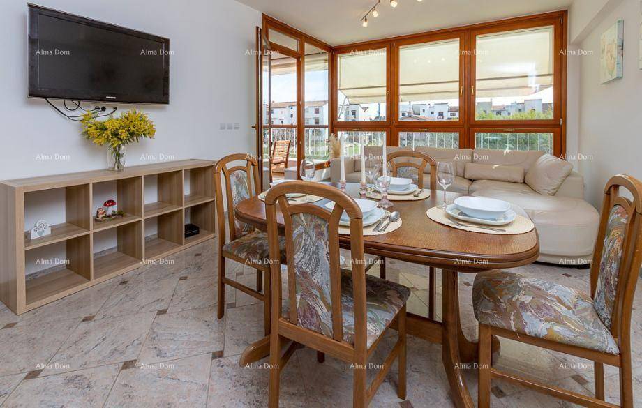 Essbereich mit Holztisch, Stühlen und Blick auf den Wohnbereich mit Fernseher und großen Fenstern.