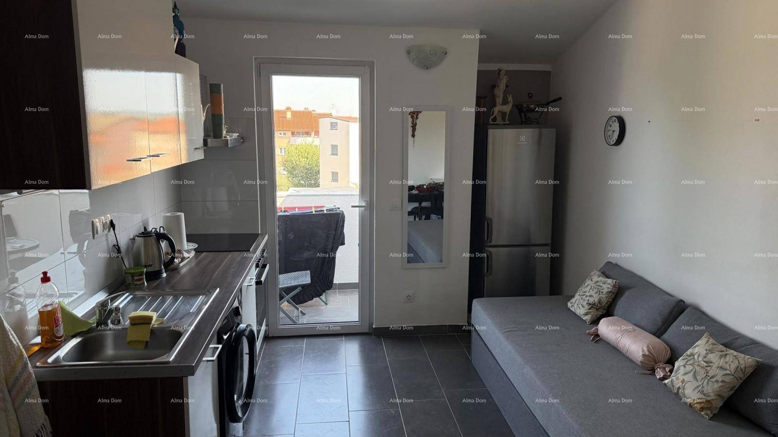 Heller Wohn- und Küchenbereich mit Sofa, Küchenzeile und Balkonzugang, ausgestattet mit dunklen Fliesen.
