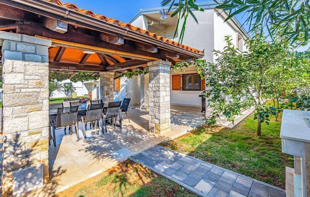 Überdachte Terrasse mit Steinsäulen, Holzbalken und einem Esstisch im Freien, umgeben von Grün.