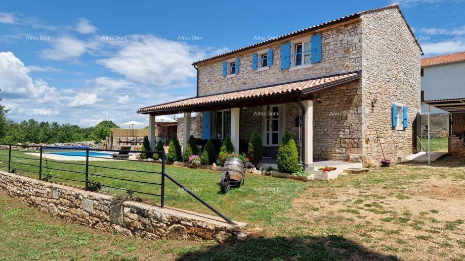 Charmantes Steinhaus mit überdachter Veranda, umgeben von einem gepflegten Garten und Pool im Hintergrund.