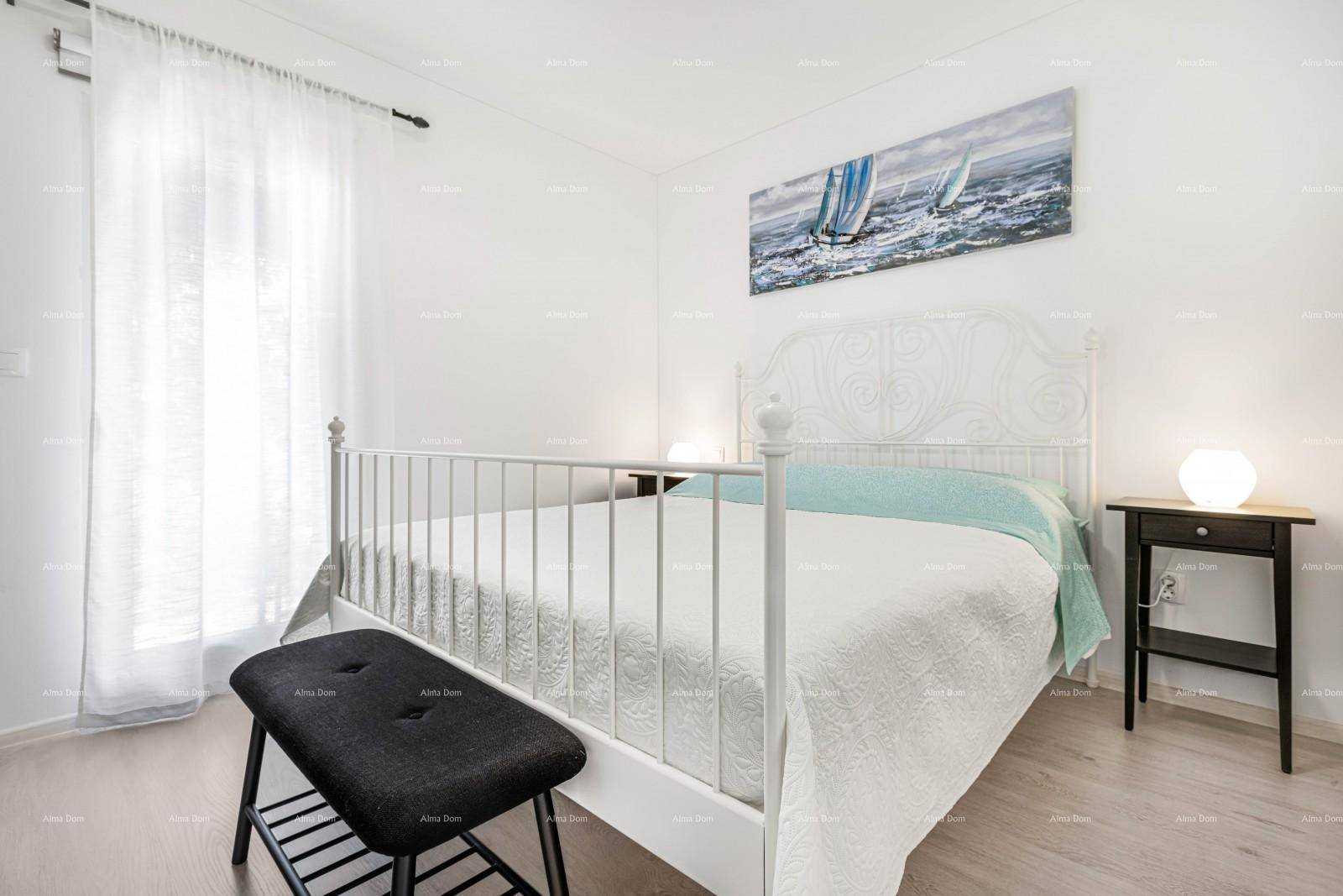 Schlafzimmer mit weißem Metallbett, hellem Boden und großen Fenstern mit Vorhängen.