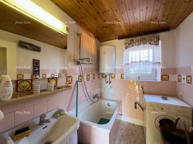 Badezimmer mit rosa-weißen Fliesen, Badewanne mit Duschfunktion, Waschbecken und Waschmaschine.